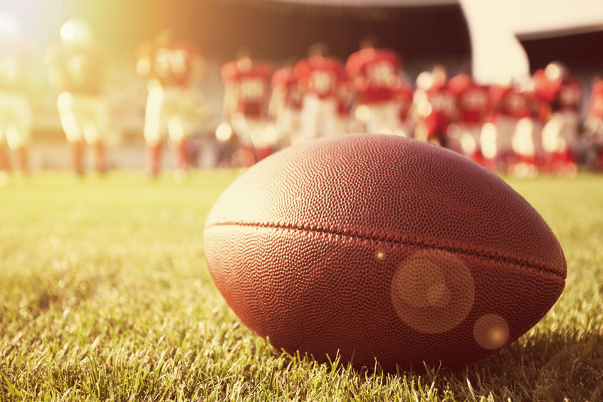 Close up of an American football with high school players warming up in the background